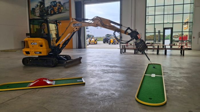 Minibagger mit Golfschläger an einer Minigolfbahn in einer Maschinenhalle